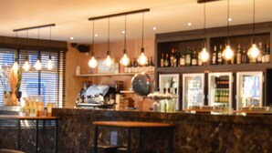 Eine Bar mit hängenden Lampen, einer Theke mit Flaschen und Sitzgelegenheiten.