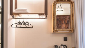 A compact hotel room with a wooden desk, a compact refrigerator, a coffee maker, and a mirror with an ornate frame.