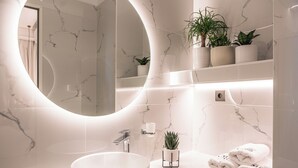 A modern bathroom with a round mirror, a white sink, and a marble backsplash.