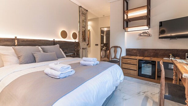 A modern hotel room with a large bed, a desk, a chair, a TV, and a small kitchenette. - Silo Luxury Rooms Nafplio (Argos - Mykines)