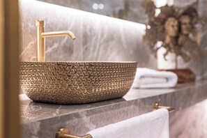 Un lavabo doré à texture particulière, surmonté d’un robinet doré, le tout posé sur un comptoir en marbre.