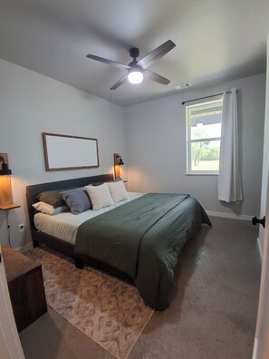 A bedroom with a bed, a ceiling fan, a window with curtains, and a wall-mounted light fixture. - Play Hard, Rest Easy. Comfortable Home Near Rocker B (Graford)