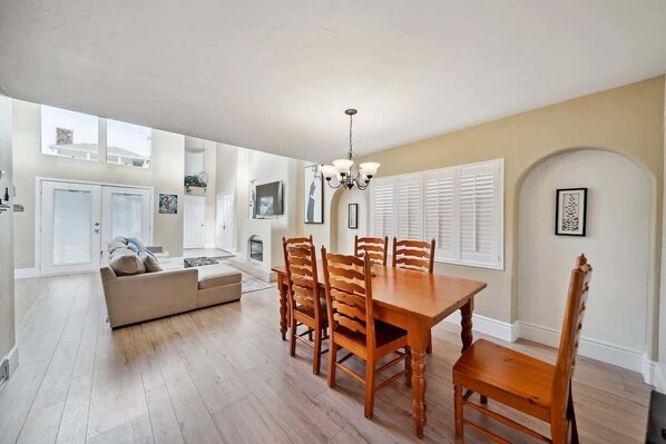 A dining area with a wooden table and chairs, a chandelier, and a sofa in the adjacent living room.