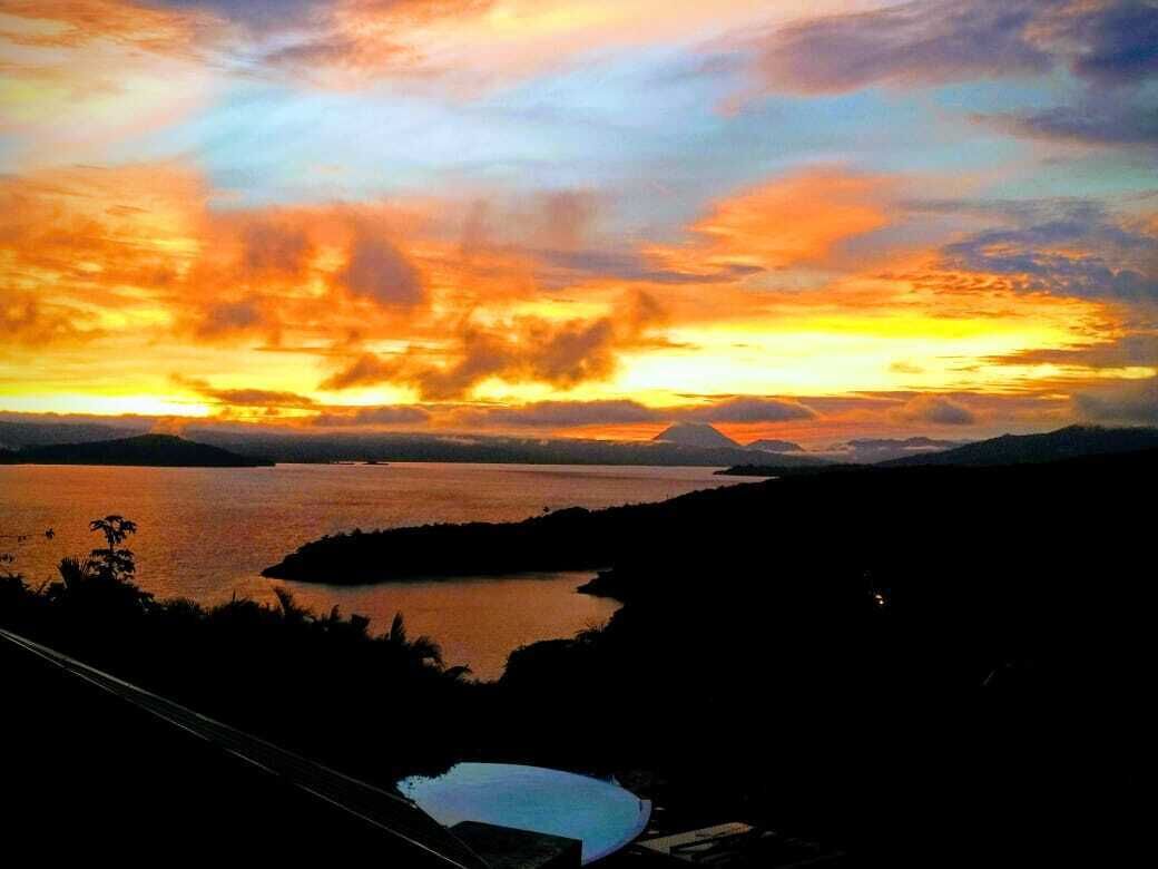A sunset view over a body of water with distant mountains, a small island, and a clear sky.