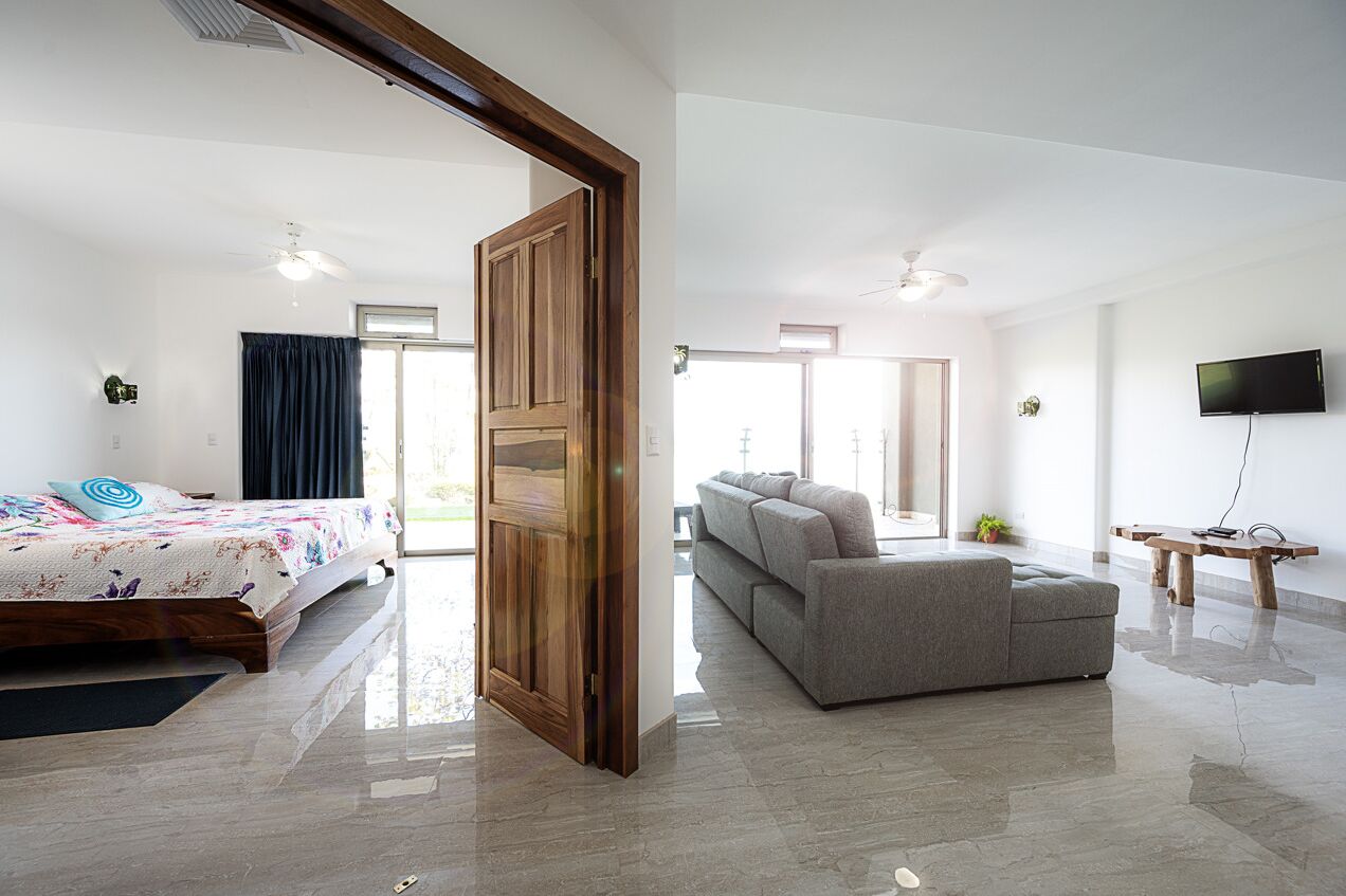 A modern hotel room with a bed, a sofa, a TV, and a wooden door.