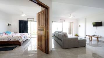 A modern hotel room with a bed, a sofa, a TV, and a wooden door.