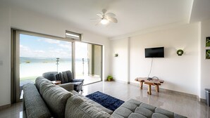 Ein modernes Wohnzimmer mit großem Fenster, Deckenventilator, Flachbildfernseher und Holztisch.