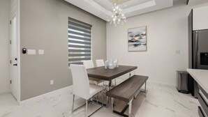 Cozinha moderna com área de refeições, piso de mármore, lustre e uma grande janela com persianas.