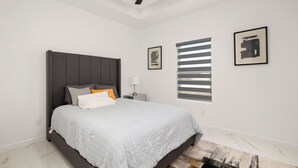 Quarto com cama, ventoinha no teto, mesa de cabeceira e duas fotos emolduradas na parede.
