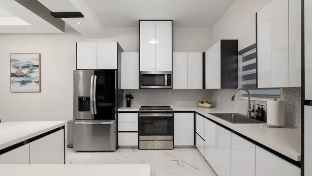 Cozinha moderna com eletrodomésticos de aço inoxidável, armários brancos e piso de mármore.