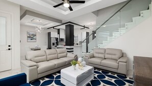 Uma sala de estar moderna com dois sofás bege, uma mesa de centro branca e um tapete azul estampado.
