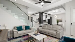 Ein modernes Wohnzimmer mit Treppe, zwei Sofas, einem Couchtisch und einem farbenfrohen Teppich.