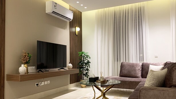 Ein modernes Wohnzimmer mit Flachbildfernseher, Glastisch, einer Couch und einer Topfpflanze.