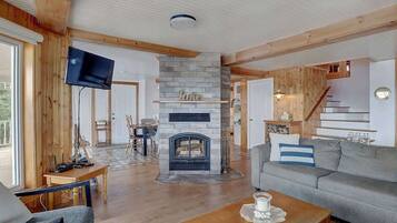 A cozy living room with a fireplace, wooden beams, a flat-screen TV, and a staircase leading to an upper level.