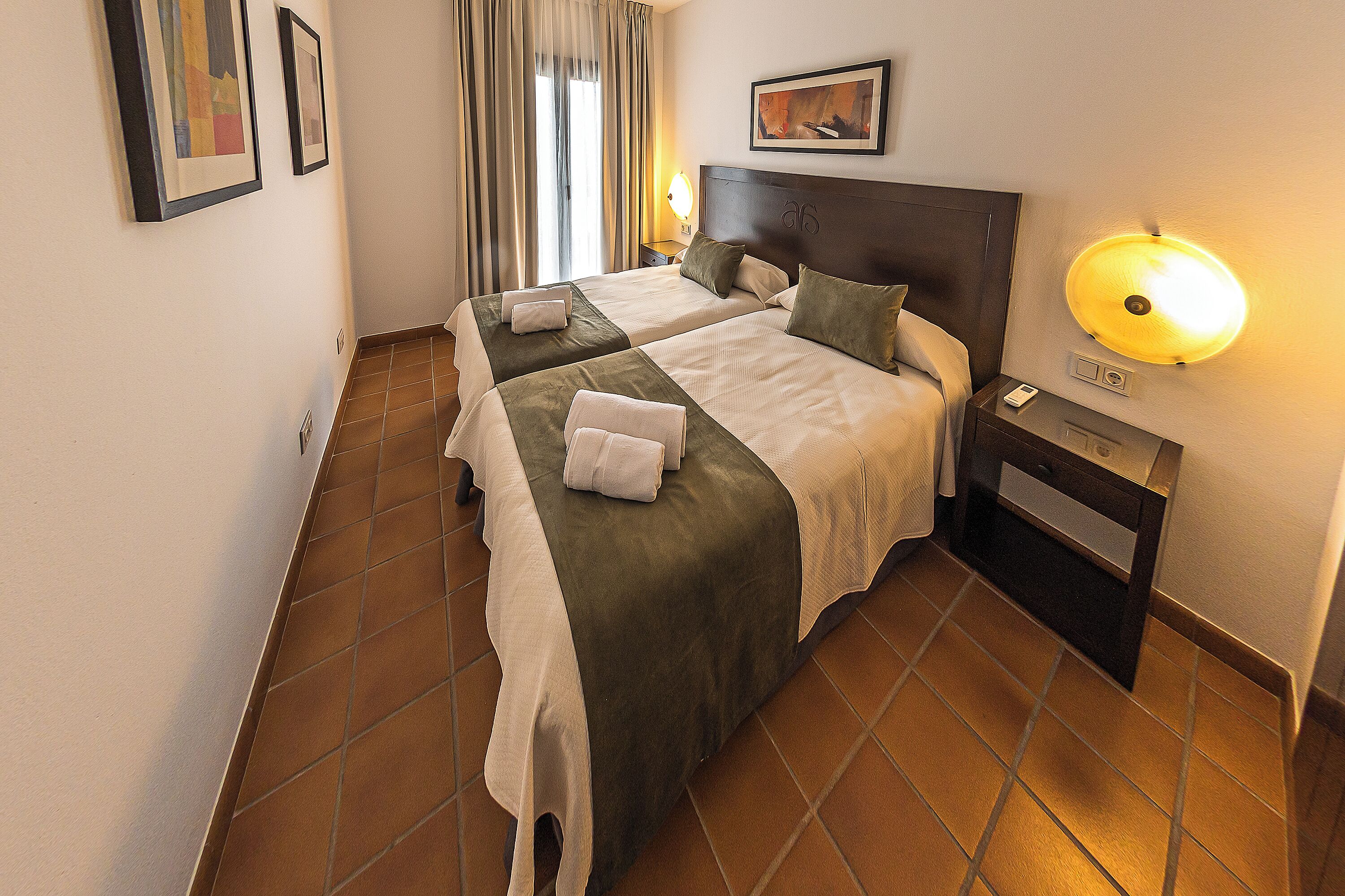 Ein Hotelzimmer mit zwei Betten, einem Nachttisch, einer Lampe und Bildern an den Wänden.