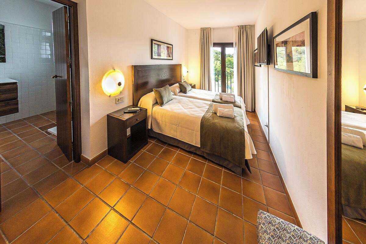 A hotel room with two beds, a bathroom, and a balcony.