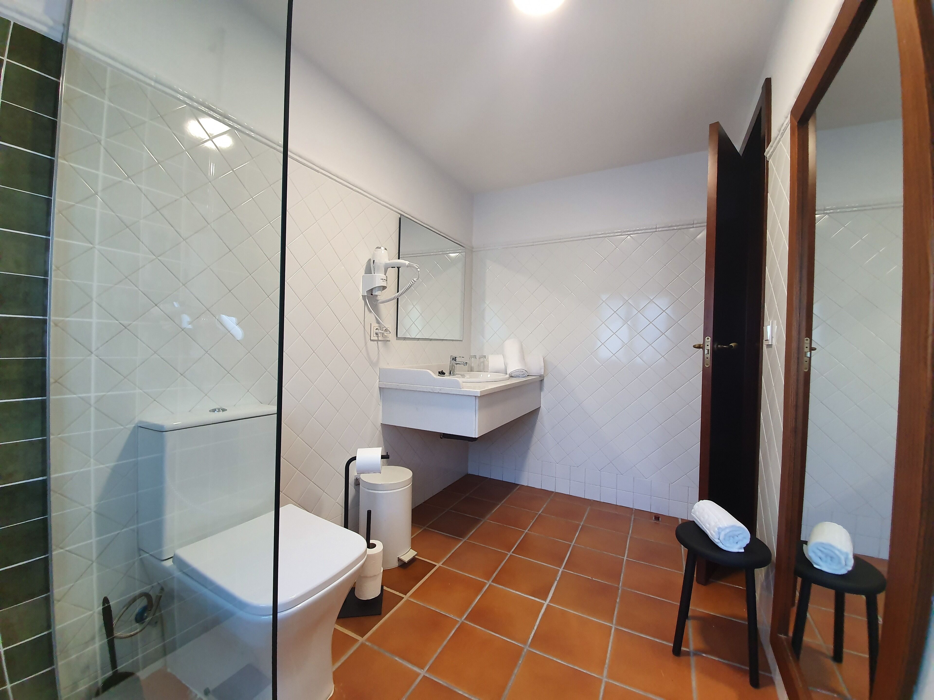 A bathroom with a toilet, sink, and mirror. There is a towel rack with towels and a trash can.