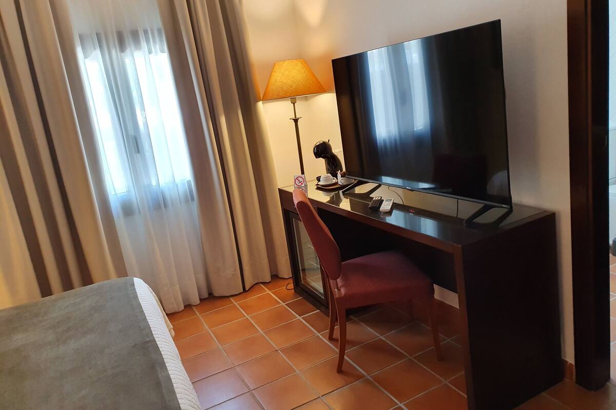 A hotel room with a bed, a desk with a TV, a lamp, and a chair.
