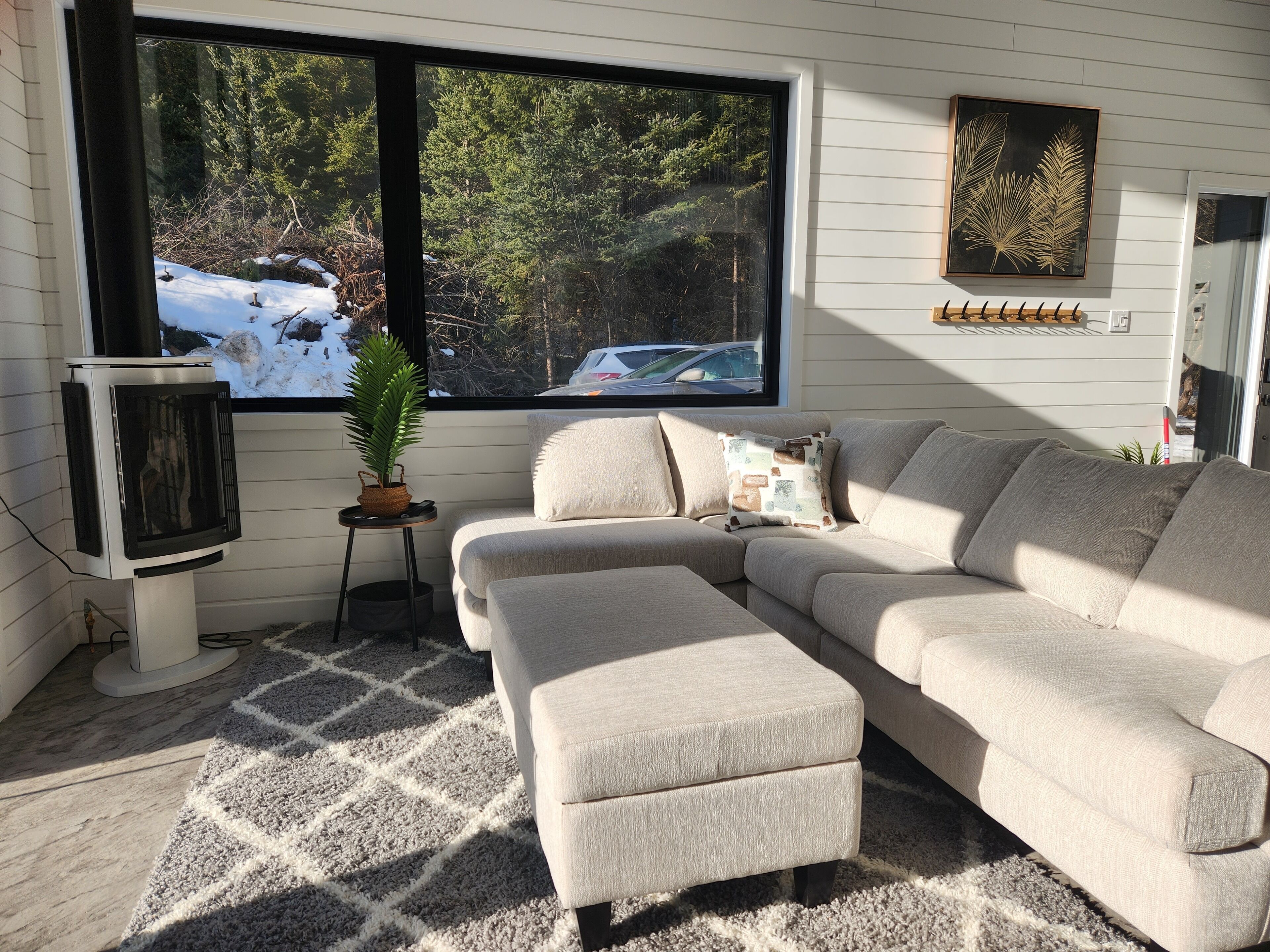 A cozy living room with a sectional sofa, a fireplace, and a large window offering a view of a snowy landscape.