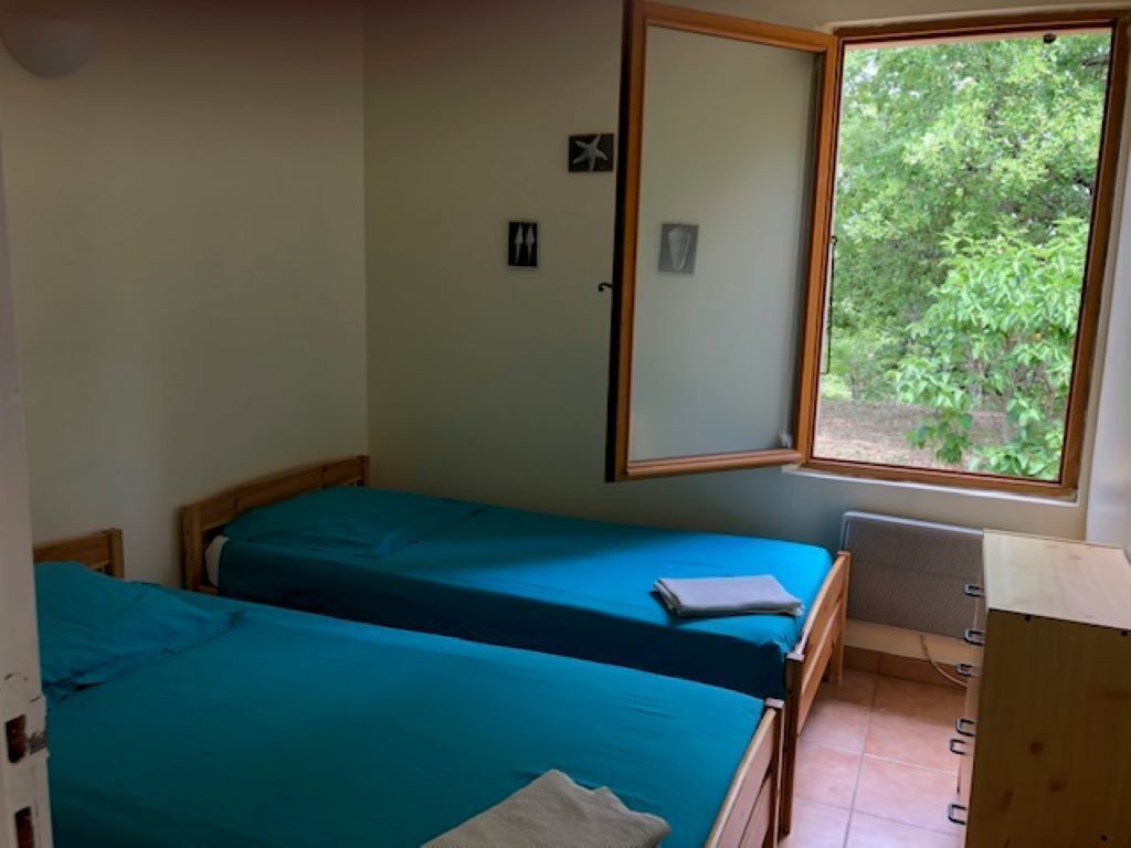 A room with two single beds, a window with a view of greenery, and a small desk with a chair.