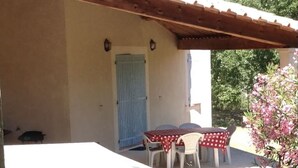 A covered outdoor patio with a table and chairs, a blue door, and a wooden pergola. - Luberon - Vue Exceptionnelle - Location de Maisonnette 4 Personnes (Ménerbes)