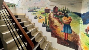 Una escalera con un mural que representa una escena campestre, incluyendo a una mujer y un perro.