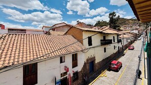 Una calle adoquinada estrecha flanqueada por edificios tradicionales con tejados de teja, cielo azul despejado y algunos coches estacionados a lo largo de la calle.