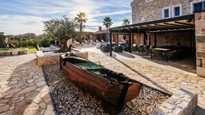 A stone patio with a boat, outdoor seating, and a stone building with windows. - Villa Marta Zadarvillas (Nin)