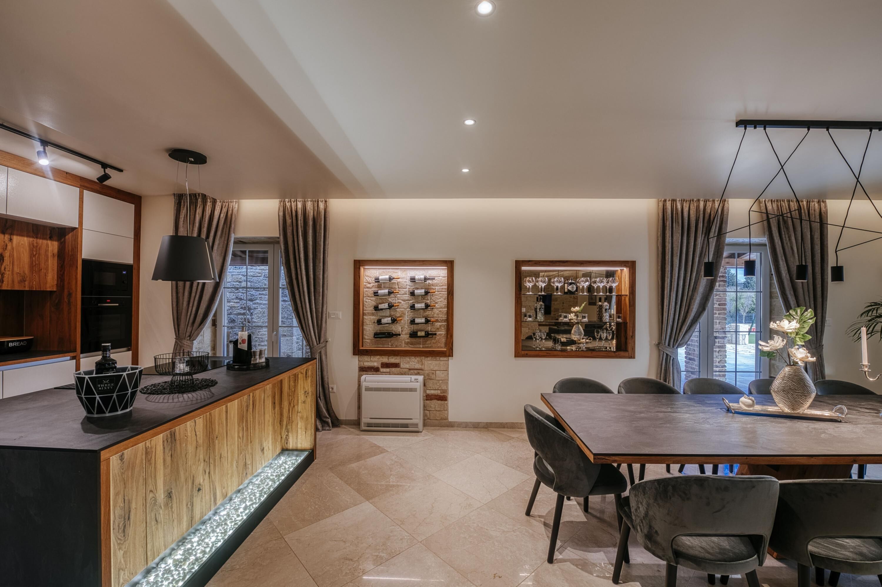 A modern kitchen with a wooden island, a dining area with a large table and chairs, and a wine rack on the wall.