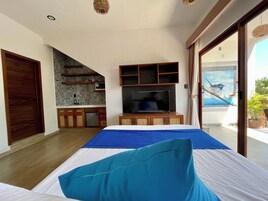 Un dormitorio con cama, televisión, kitchenette y balcón con vista al mar.