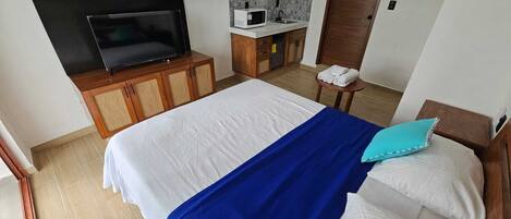 Une chambre d’hôtel avec un lit, un téléviseur posé sur un meuble en bois, un four à micro-ondes et une petite table avec des serviettes.