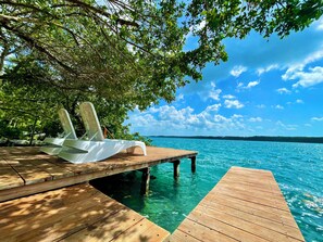 A wooden deck extending over clear blue water, with a white lounge chair under a tree. - Estancia del Agua Luxury View (Xul-Ha)