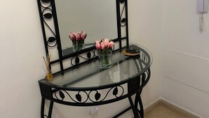 Et spejl med sort ramme, en vase med lyserøde blomster og en telefon på væggen.