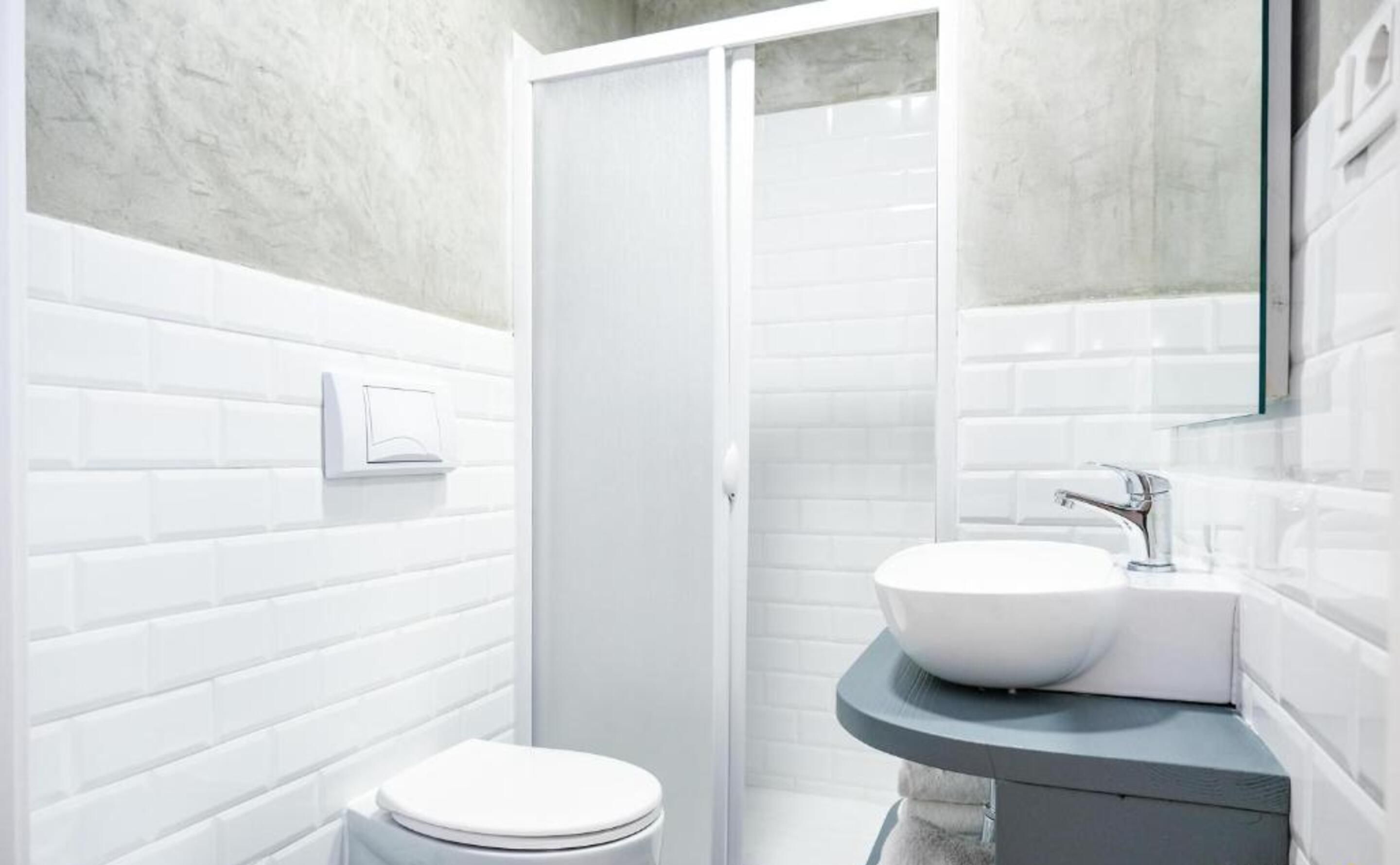 Un baño moderno con azulejos blancos tipo metro, inodoro blanco, cabina de ducha y tocador con lavabo y espejo.