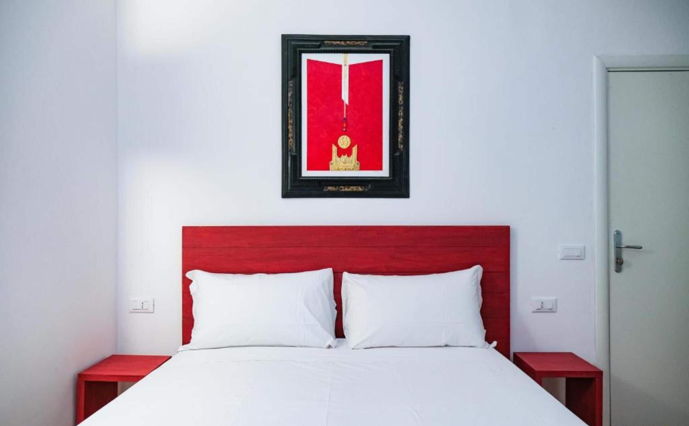 A hotel room with a red headboard, white bedding, and a framed picture on the wall.