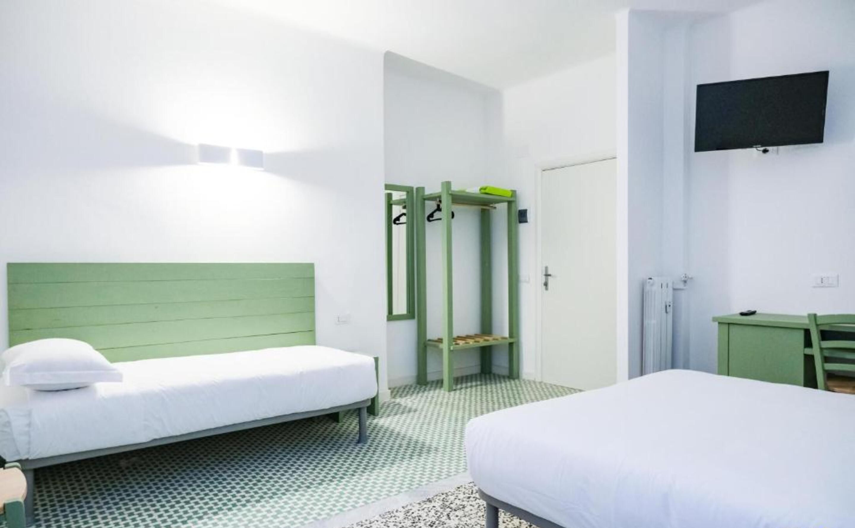 Een hotelkamer met twee bedden, een groen hoofdeinde, een aan de muur bevestigde televisie en een douche.