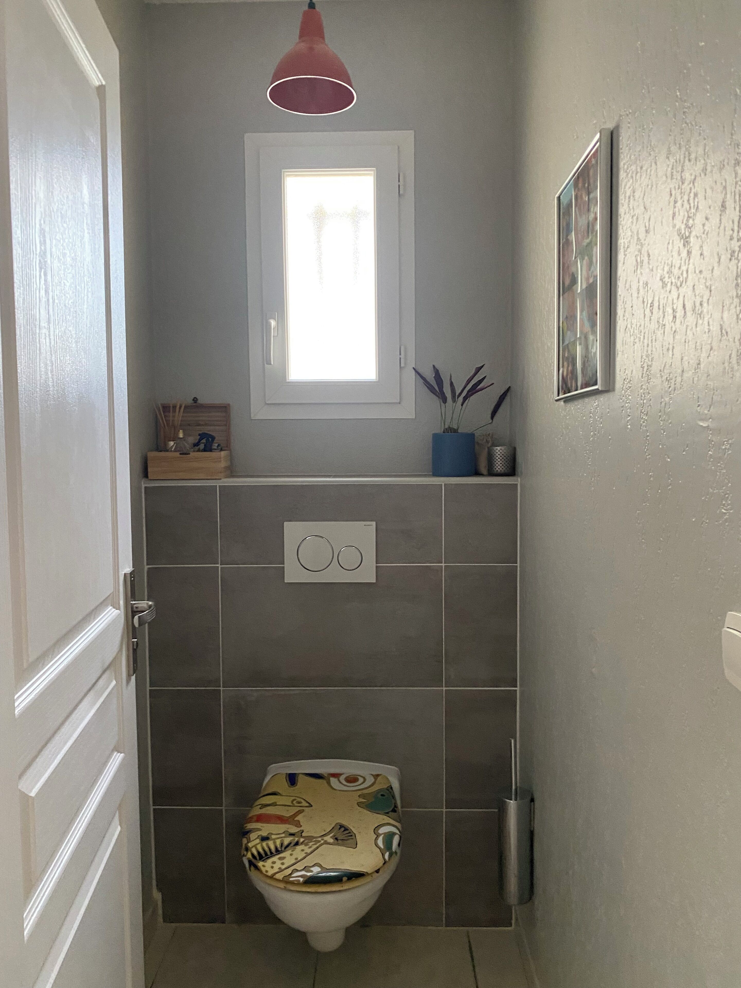 Un baño con inodoro, una ventana y una lámpara colgante roja.