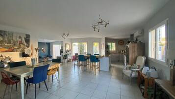 Een ruime woonkamer met een eettafel, stoelen en een keuken, met een groot raam.