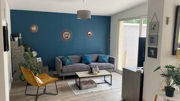Een moderne woonkamer met een blauwe accentmuur, een grijze bank, een houten salontafel en een gele fauteuil.
