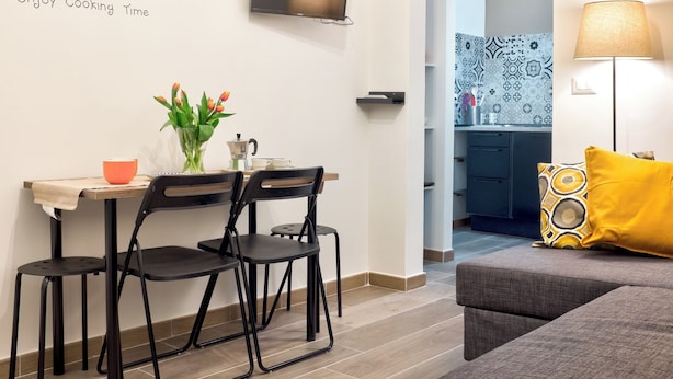 A modern kitchen with a dining area, a TV mounted above the counter, and a sofa with a yellow pillow. - Manuela Apartments 1 Plebiscito Quartieri Spagnoli (Naples)