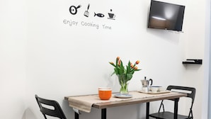 A dining area with a table set for two, a TV mounted on the wall, and a wall decoration with cooking utensils and the phrase "Enjoy Cooking Time". - Manuela Apartments 1 Plebiscito Quartieri Spagnoli (Naples)