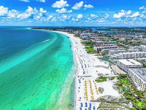 An aerial view of a coastal city with a wide beach, clear turquoise waters, and a mix of residential and hotel buildings. - Beautiful Two Bedroom/ Two Bath Bianco Sands, Quick Walk to Beach! (Siesta Key)