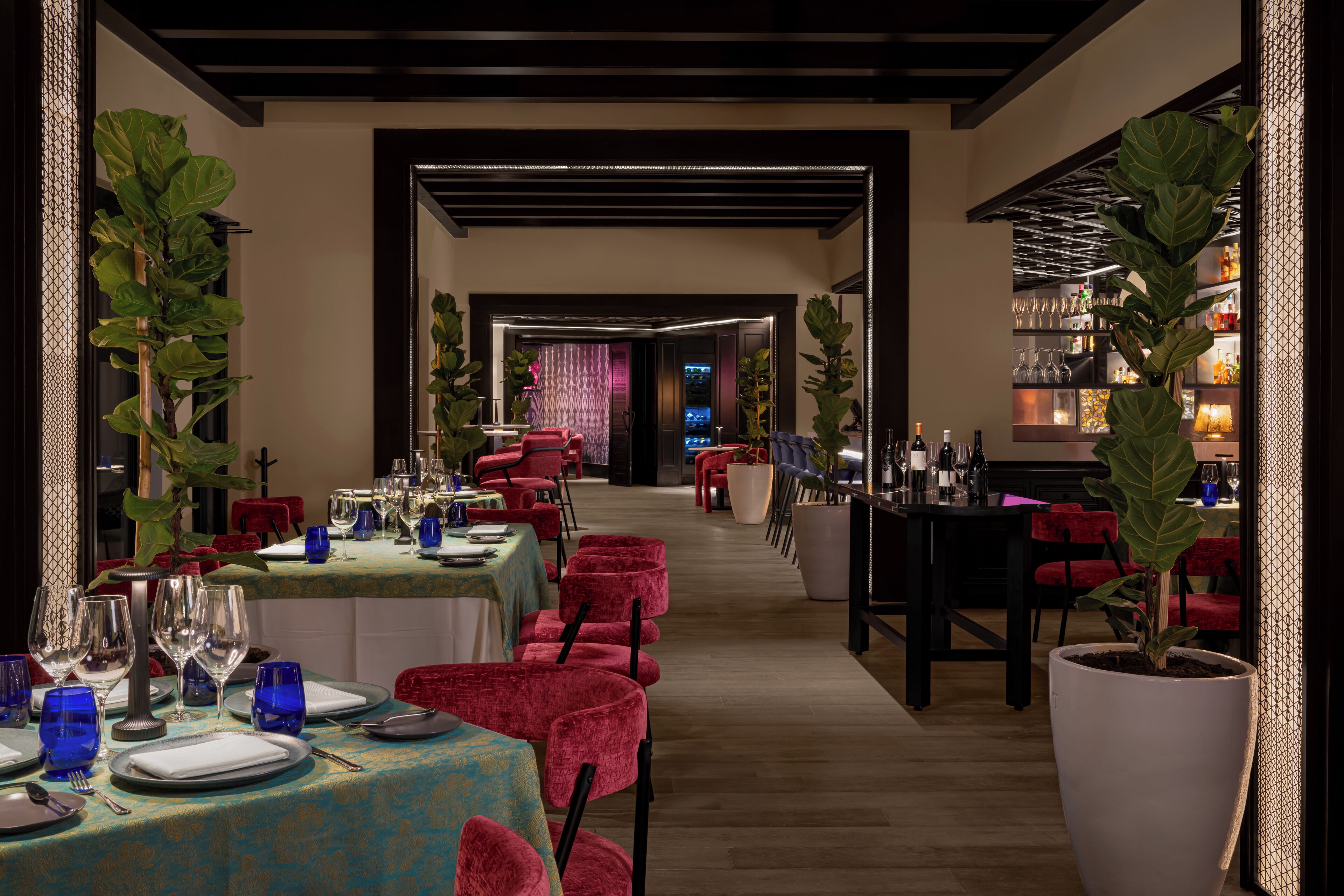 Un restaurante con mesas dispuestas para comer, sillas rojas y plantas en macetas.