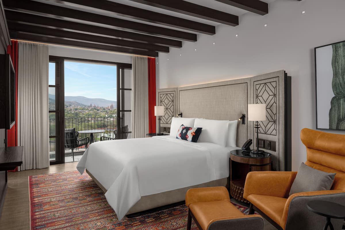 Ein Hotelzimmer mit einem großen Bett, einer Couch, einem Schreibtisch und einem Balkon mit Blick auf die Stadt.