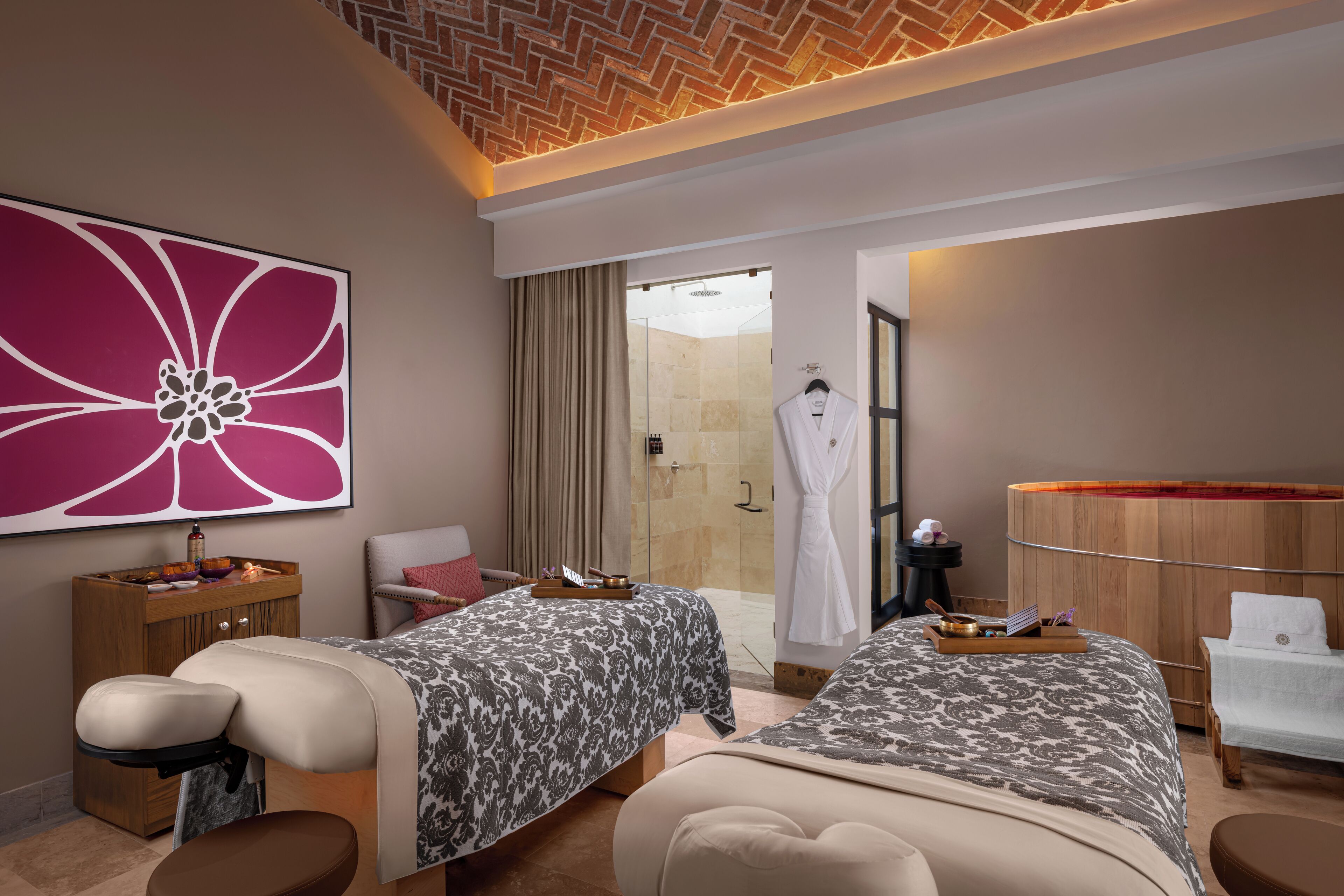 A hotel room with two beds, a massage chair, a wooden cabinet, a large flower painting, and a glass shower area.