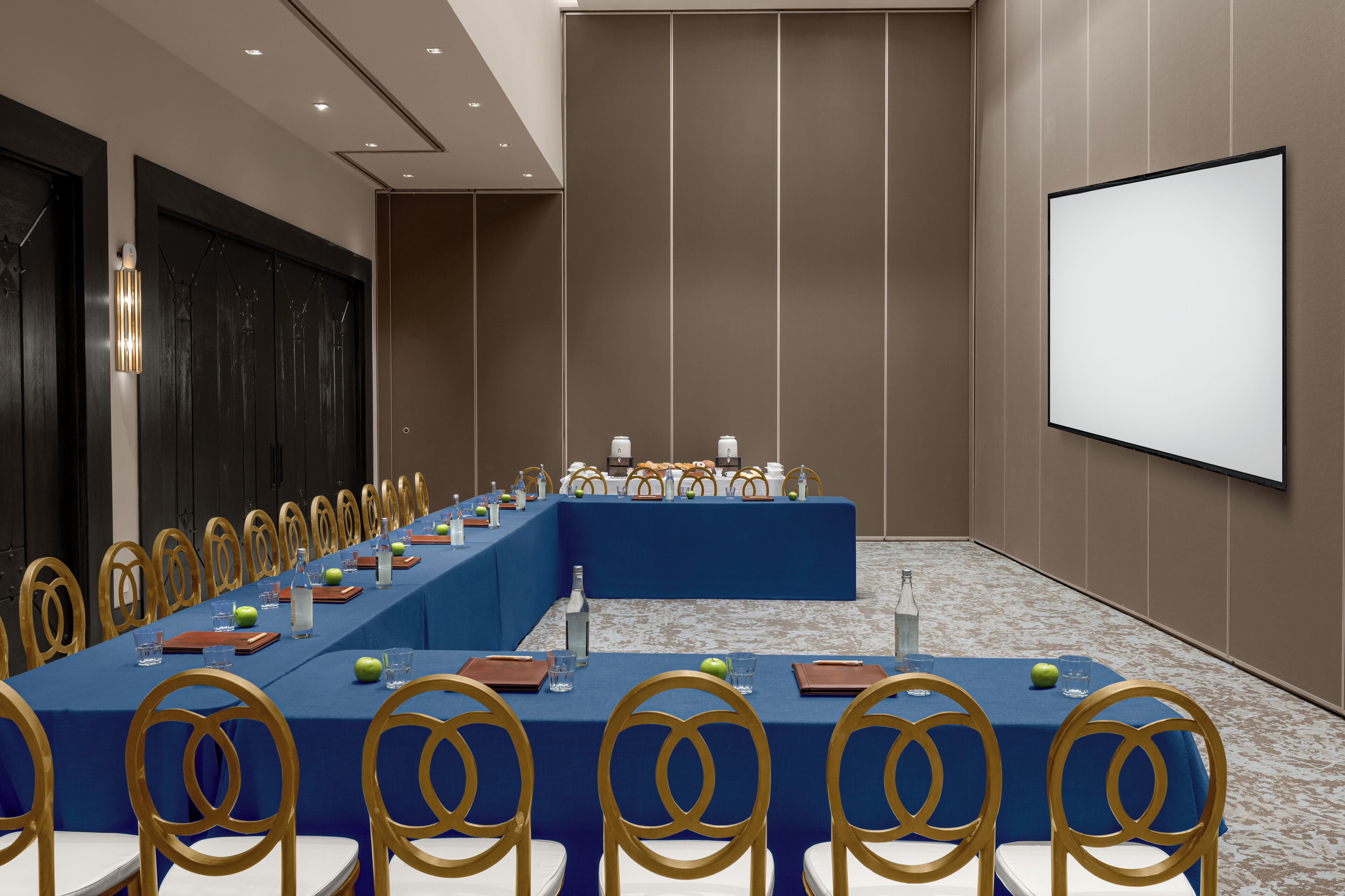 A conference room with a long table, chairs, a screen, and a projector.