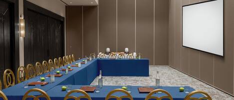 A conference room with a long table, chairs, a screen, and a projector.