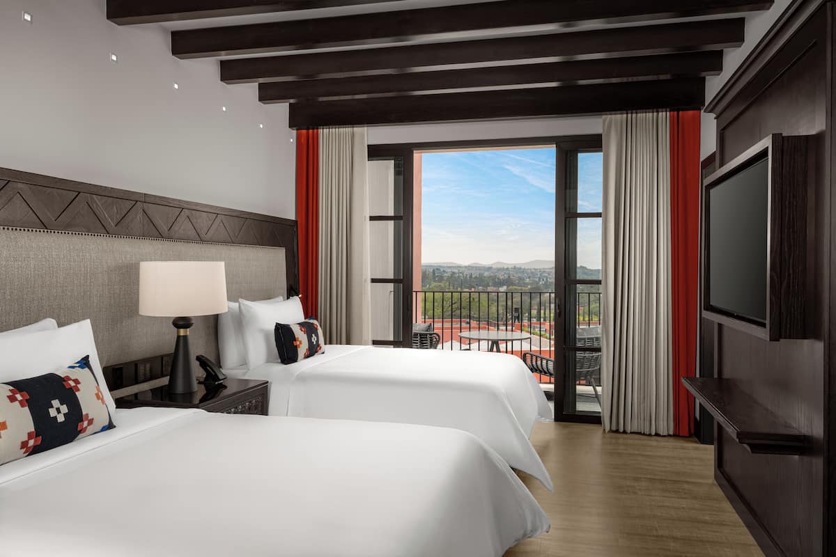 Ein Hotelzimmer mit zwei Betten, einem Fernseher und einem Balkon mit Blick auf die Stadt.