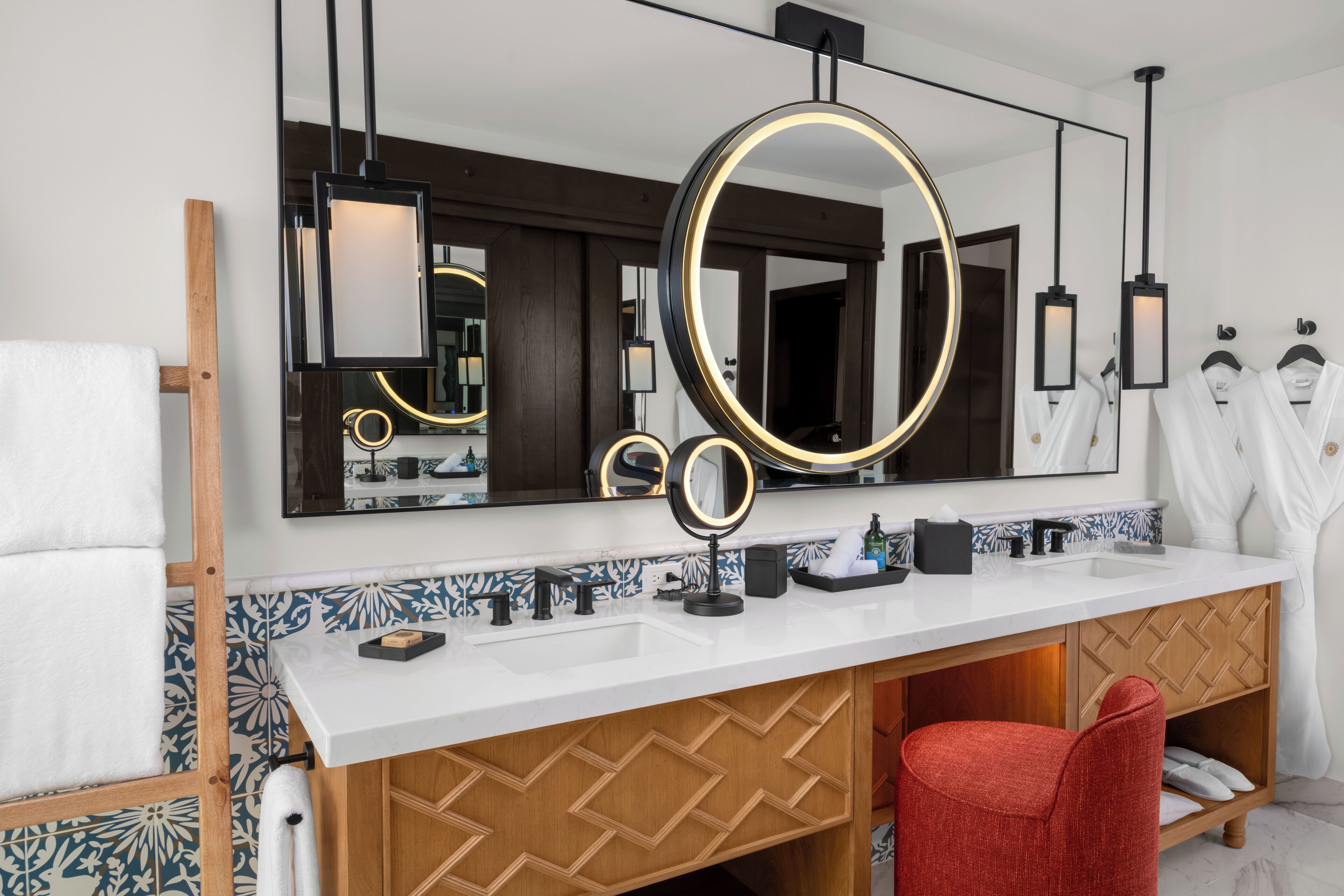 A modern bathroom with a large mirror, two sinks, a vanity, and a red chair.