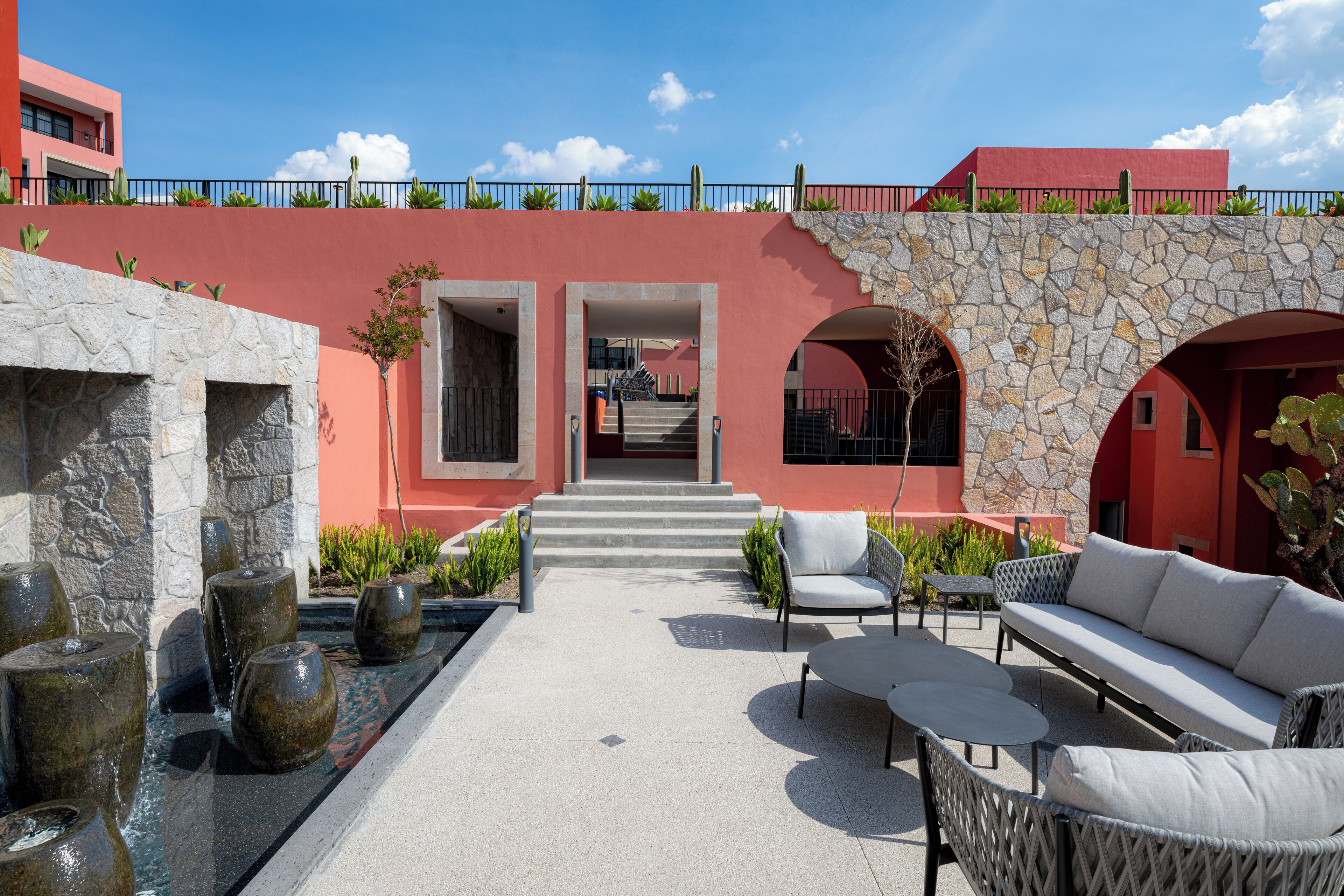 A courtyard with a stone wall, a white sofa, and a staircase leading to an upper level.